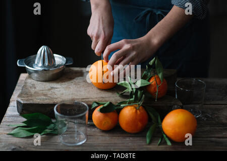 Die Hände des jungen Mannes schneiden Orangen Stockfoto