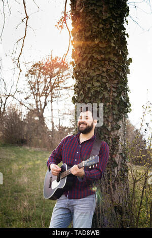 Mann Gitarre zu spielen, ein Baum auf der Wiese Stockfoto