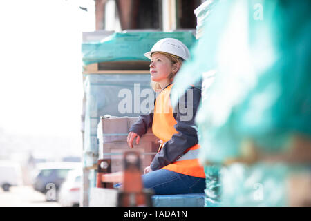 Frau mit Warnweste und Helm sitzen auf Baumaterial Stockfoto
