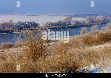 Trocken goldene Gras und Sträuchern auf die Banken und die Hänge der südlichen Bug schlängelnden Fluss vor dem Hintergrund der schneebedeckten Feld und eine Eisenbahn Stockfoto