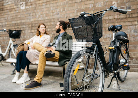 Paar auf einer Bank sitzen neben e-bikes sprechen Stockfoto