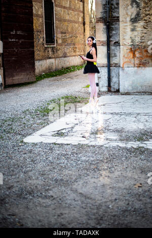 Italien, Verona, Frau im Ballett Kleid mit Handy und Kopfhörer an einem alten Gebäude Stockfoto