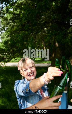 Portrait von Frau klirren Bier Flasche mit Freunden im Park Stockfoto