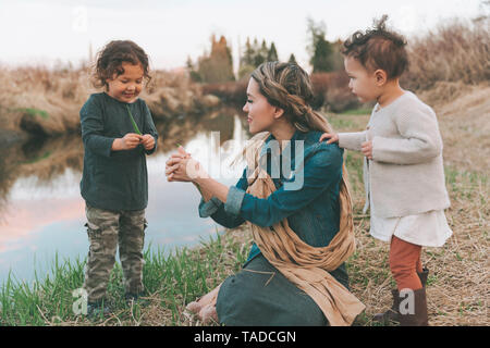 Maother und Kinder spielen mit einem Gras Blade an einem Fluss Stockfoto