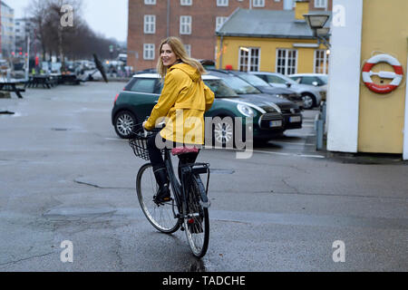 Dänemark, Kopenhagen, glückliche Frau Reiten Fahrrad auf der Uferpromenade in regnerischen Wetter Stockfoto