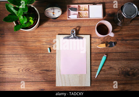 Clip Board mit leeren rosa Papier, Kaffeebecher und andere Utensilien auf dem Schreibtisch im Büro zu Hause, Ansicht von oben Stockfoto