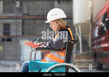 Frau mit Warnweste und Helm sitzt im Rollstuhl Notizen Stockfoto