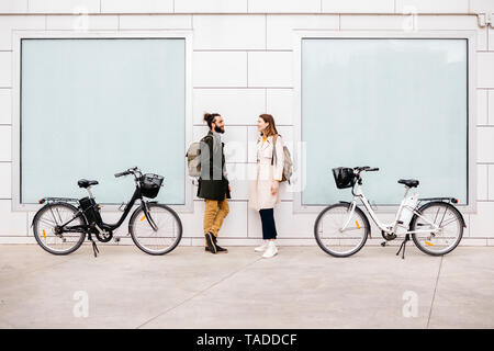 Mann und Frau mit e-bikes stehen an einem Gebäude sprechen Stockfoto