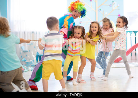 Begeistert Kinder und Clown spielen Tauziehen im Club Stockfoto