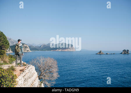 Ein Tourist mit einem Rucksack auf einer Klippe oder Hügel neben das Meer in die Ferne schaut. Allein reisen. Stockfoto