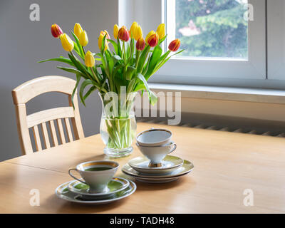 Blumenstrauß aus roten und gelben Tulpen am Esstisch mit Kaffeetassen Stockfoto