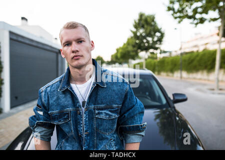 Portrait des jungen Mannes in Jeans Jacke, der vor dem Auto Stockfoto