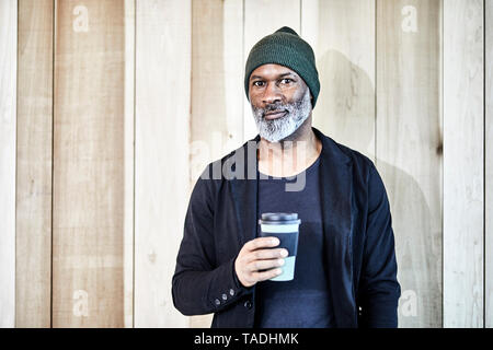 Portrait von zuversichtlich reife Kaufmann mit Kaffee zum Mitnehmen an der hölzernen Wand Stockfoto