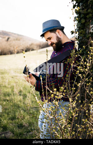 Mann Gitarre zu spielen, ein Baum auf der Wiese Stockfoto