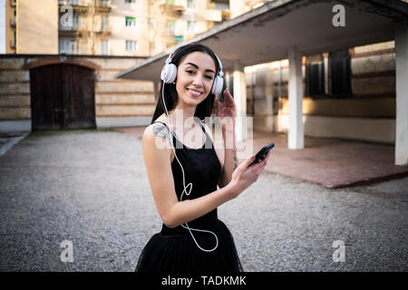 Italien, Verona, Porträt der lächelnde Frau im Ballett Kleid mit Handy und Kopfhörer Stockfoto