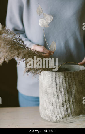 Eine Frau, die Blumen und Gräser in einer Vase arrangiert Stockfoto