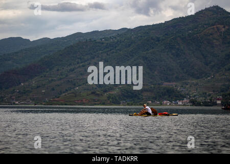 Junger Mann Rudern auf dem paddleboard durch Hund im See von Pokhara in Nepal begleitet. Barahi Mandir Phewa Tal Phewa See Stockfoto