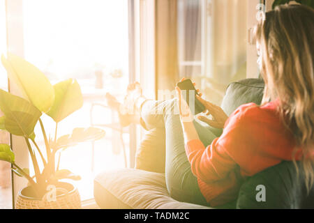 Frau im Sessel zu Hause mit Handy Stockfoto