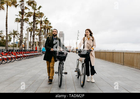 Paar drücken e-Bikes auf der Strandpromenade Stockfoto