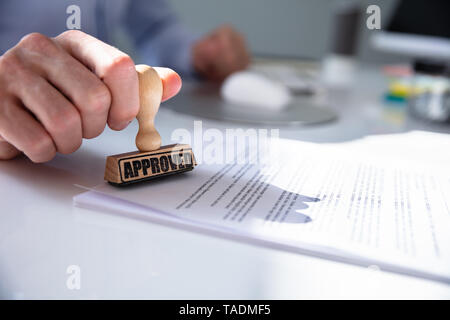 Nahaufnahme von einer Person Hand Stanzen mit Genehmigt Stempel auf Dokument am Schreibtisch Stockfoto