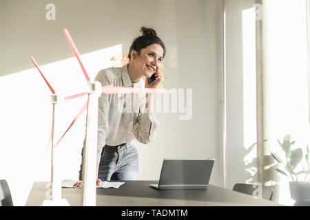 Geschäftsfrau mit wind turbine Modelle und Laptop auf dem Schreibtisch im Büro sprechen über Handy Stockfoto