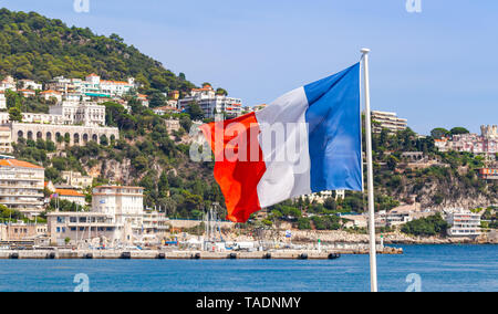 Flagge Frankreich wellenartig auf Wind über verschwommenes Küstenlandschaft Hintergrund. Französische Riviera, Nizza, Frankreich Stockfoto