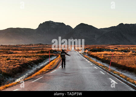 Norwegen, Lofoten, Rückansicht des Menschen per Anhalter auf leere Landstraße Stockfoto