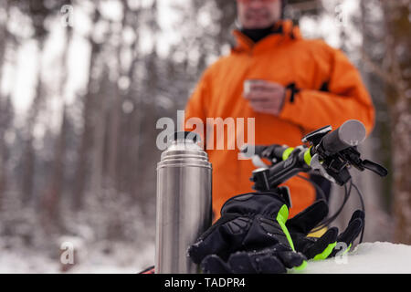 Mann, der einen Bruch von Mountainbike Reise im Winter Wald in einem heißen Getränk Stockfoto