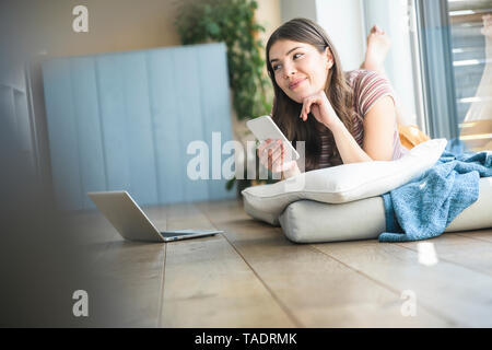 Junge Frau am Fenster zu Hause holding Handy liegen Stockfoto