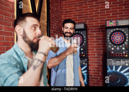 Zwei glückliche Freunde trinken Bier an der Dartscheibe in einem Pub Stockfoto