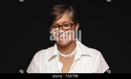 Nahaufnahme von gerne ältere Frau in Brillen lachen. Ältere Frau lachend mit geschlossenen Augen auf schwarzem Hintergrund isoliert. Stockfoto