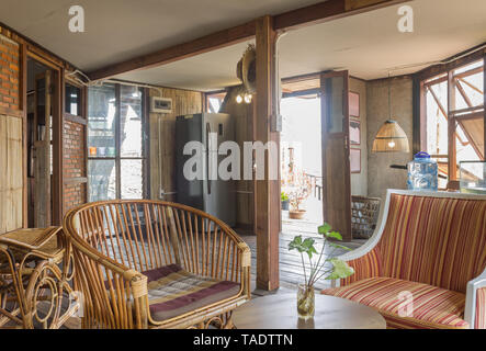 Rattan Stuhl und Sessel und Kühlschrank im Land Loft Innenarchitektur Zimmer. Interior Design Zimmer gehören Lampe und Tür und Fenster und Wand Stockfoto