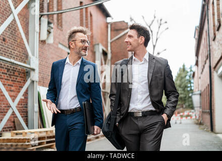 Zwei lächelnde Geschäftsleute zu Fuß und im Gespräch mit einem alten Backsteingebäude Stockfoto