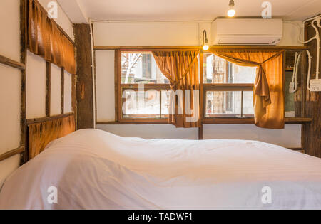 Weiß Bett im Schlafzimmer im Loft Innenarchitektur Zimmer von der Seite. Interior Design Zimmer gehören Lampe und Klimaanlage und Fenster. Interior Design Stockfoto