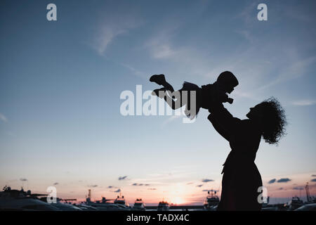 Silhouette der Mutter spielt mit ihrer Tochter bei Sonnenuntergang Stockfoto