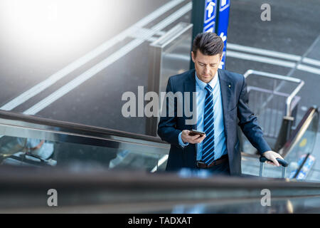 Geschäftsmann mit Koffer und Handy auf Rolltreppe Stockfoto