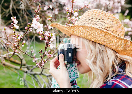 Junge Frau mit einem Strohhut Aufnehmen von Bildern im Garten mit einer alten Kamera Stockfoto