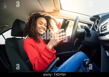 Glückliche junge Frau mit Handy im Auto Stockfoto