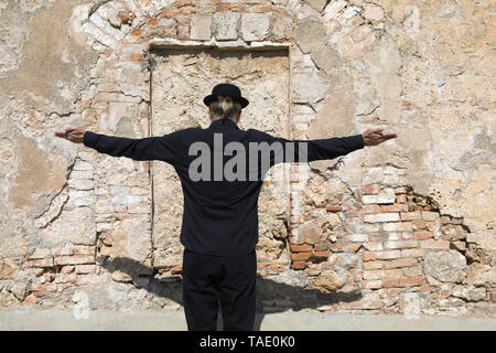 Rückansicht der Mann mit dem Hut bei Steinwand mit ausgestreckten Armen Stockfoto