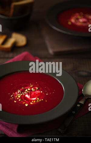 Gesunde rote Rüben Suppe oder Smoothie mit gehackten Pistazien und saure Sahne in die schwarze Platte im rustikalen Stil dekoriert. vegetarisches Mittagessen oder Abendessen Stockfoto
