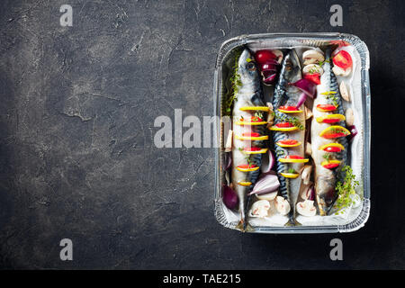 Ganze drei raw Makrele mit Zitronen, Tomaten, Pilze, Gewürze und Kräuter. scomber Bereit zum Grillen in Aluminium Rechteckige Backform auf Beton Stockfoto