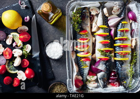 Ganze drei Makrelen mit Zitronen, Tomaten, Pilze, Gewürze und Kräuter. scomber Bereit zum Grillen in Aluminium Backform auf einer konkreten Tabelle mit Stockfoto