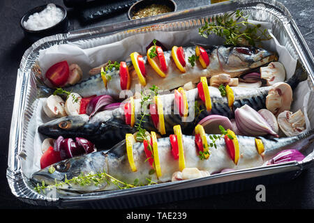 Ganze drei raw Makrele mit Zitronen, Tomaten, Pilze, Gewürze und Kräuter. scomber zum Grillen in Aluminium Backform auf einer konkreten Tabelle vorbereitet, Stockfoto