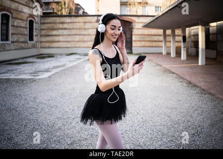 Italien, Verona, lächelnde Frau im Ballett Kleid mit Handy und Kopfhörer Stockfoto