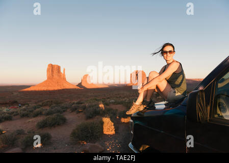 USA, Utah, Monument Valley, Frau sitzt auf der Motorhaube, genießen den Sonnenuntergang im Monument Valley Stockfoto