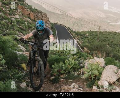 Spanien, Lanzarote, Mountainbiker sein Rad schieben ein Wanderweg in die Berge Stockfoto