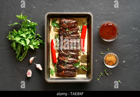 Gebratene Rippchen in Backblech über schwarzen Stein. Leckere bbq-Fleisch. Ansicht von oben, flach Stockfoto