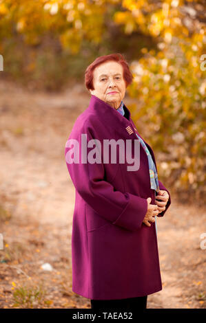 Lächelnd senior Frau 70-80 Jahre alten tragen stilvolle Wintermantel posiert in Park. Mit Blick auf die Kamera. Wellness. 80 s. Stockfoto
