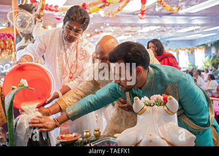 Ein Teenager Pandit und zwei fromme Gläubige gießen Sie Milch über, und tippen Sie auf einen Shiva Lingam an einem Hindu Tempel in Jamaica, Queens, New York. Stockfoto