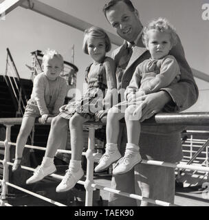 1950er historischen, gut gekleideten Vater mit seinen drei Kinder draußen Sitzen auf dem Geländer auf dem Deck eines Union-Castle Dampfschiff auf dem Ozean unterwegs zum Kap in Südafrika ein neues Leben zu beginnen. Stockfoto